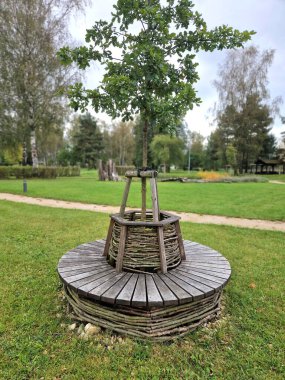 Tahta panelli, gri metal plakalı bir bankta oturuyordu. Parktaki çimlerin etrafındaki çakıl harman yolunun etrafında üç koltuk vardı.