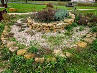 Bir çiçek tarlasında merdivenleri olan kumtaşı duvarlar ve taşlar. Çiçekli kaya bahçeleri ve çakıl yüzeyi olan merdivenler. Bitki bahçesi, mermer, lavanta, kütük, yükseltilmiş yatak.