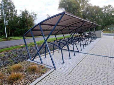 Noktalı cam çatılı bisiklet parkı. Bükülmüş gri borulardan, şehir parkındaki metal saplara bağlı gri sertleştirilmiş camlara kadar. plastik