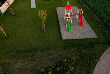 sandy children playground bordered by tree trunks and sandstone boulders. a very natural impression of a kindergarten park. stainless steel slide and circle trampoline, boulder, trampolining