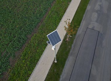 Gri paslanmaz çelik sütun silindirik şekil. Şeffaf bir kapağı ve LED lambaları olan bir lamba. Sokak lambasının üstünde küçük bir güneş paneli var. halka açık park
