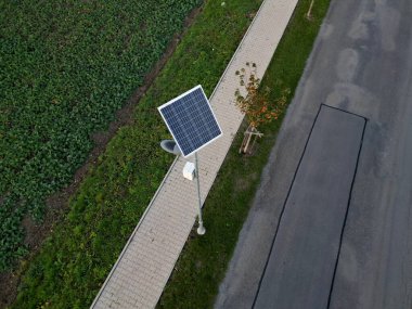 Gri paslanmaz çelik sütun silindirik şekil. Şeffaf bir kapağı ve LED lambaları olan bir lamba. Sokak lambasının üstünde küçük bir güneş paneli var. halka açık park
