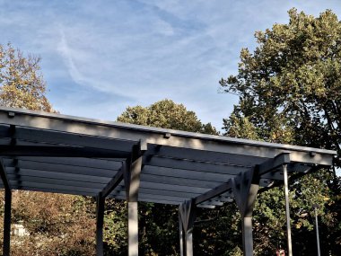 Pergola 'nın gri yapışkan ahşap yapısı düz silindirik beyaz sütunlar tarafından desteklenmektedir. Çatı kiremitlerden, cam camlardan, ağaç tepesinden, akçaağaç ağacından, büyük