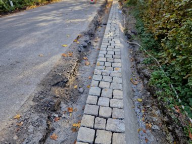 Yolun kenarı, bir ipliğe göre düz bir çizgide döşenmiş kaldırım taşlarından yapılmış taş bir sınırla şekillenir. beton çubuklar asfalt etrafında