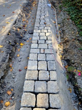Yolun kenarı, bir ipliğe göre düz bir çizgide döşenmiş kaldırım taşlarından yapılmış taş bir sınırla şekillenir. beton çubuklar asfalt etrafında