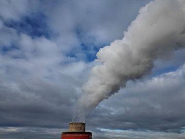 detail of a smoking industrial chimney. burning waste and gas with co2 damages the environment. a plume of vapor joins the clouds clipart