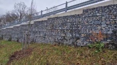 Yolun yamacını tutan çirkin beton duvar doğal taşlarla dolu bir gabionla kaplı. Astarın görünümü daha doğal.