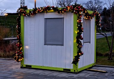 Pencereli konteynır Noel pazarları için bir yazarkasa. Kapalı bir panjuru var. Plastik bir Noel çelengi.