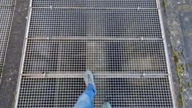 Bir adam karlı bir vadide metal bir köprüde yürüyor. galvanize metal merdiven. Kar ağların arasından düşüyor. Fabrika teknoloji kontrolü. Yapıların kaynak ve üretimi