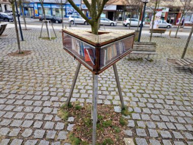 Okulun önündeki meydanda kitap saklamak için üçgen şeklinde bir dolap. Ağaç gövdesi deliğin içinden geçiyor. ücretsiz cam kitaplığı