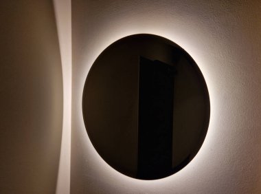 Çevresinde lamba olan dairesel ayna. Sonra arka ışıklandırması olan gri beton alçıdan basit bir ayna, karanlık bir kulüp atmosferi.