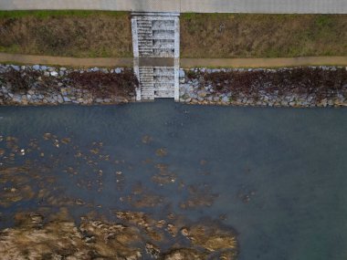 newly created natural embankment by river. benches, terraces, relaxed staircase serve people as well as fishing and relaxation. strengthening banks against water erosion by large stones on dry lined  clipart