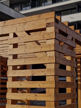 Duvarları ve çatısı çizgili ahşap pergola. Tırmanma bitkileri için çardak görevi görüyor. Kumlu bej yüzey. Tel banklarla parktaki patikalar. Vidaları ve iplikleri olan temel çubuklar, kış
