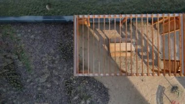 Duvarları ve çatısı çizgili ahşap pergola. Tırmanma bitkileri için çardak görevi görüyor. Kumlu bej yüzey. Tel banklarla parktaki patikalar. Vidaları ve iplikleri olan temel çubuklar, kış