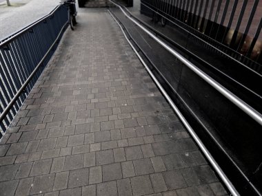 Binanın girişi tekerlekli sandalyeli engelliler için de geçerli. El ele tutuşmak için duvarda bir çubuk ve el arabasının direksiyonunun altında bir kılavuz çubuğu olan koyu renkli taş paneller..