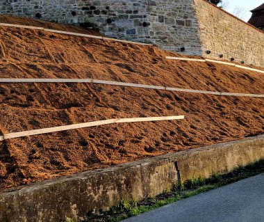 Çimento karıştırıcısının uzun düz duvarı. Duvarın arkasında duvarın içinden drenaj borularıyla çıkarılan toprak var. Kanalizasyon borusu çekiliyor. İnşaat alanı, mezarlık, gabion.