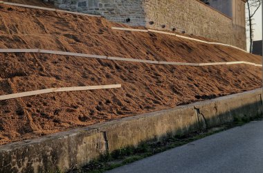 Çimento karıştırıcısının uzun düz duvarı. Duvarın arkasında duvarın içinden drenaj borularıyla çıkarılan toprak var. Kanalizasyon borusu çekiliyor. İnşaat alanı, mezarlık, gabion.