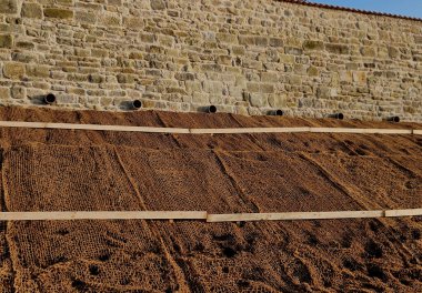 Çimento karıştırıcısının uzun düz duvarı. Duvarın arkasında duvarın içinden drenaj borularıyla çıkarılan toprak var. Kanalizasyon borusu çekiliyor. İnşaat alanı, mezarlık, gabion.