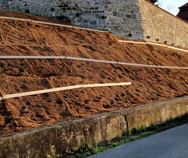 Çimento karıştırıcısının uzun düz duvarı. Duvarın arkasında duvarın içinden drenaj borularıyla çıkarılan toprak var. Kanalizasyon borusu çekiliyor. İnşaat alanı, mezarlık, gabion.