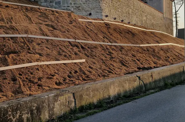 Çimento karıştırıcısının uzun düz duvarı. Duvarın arkasında duvarın içinden drenaj borularıyla çıkarılan toprak var. Kanalizasyon borusu çekiliyor. İnşaat alanı, mezarlık, gabion.