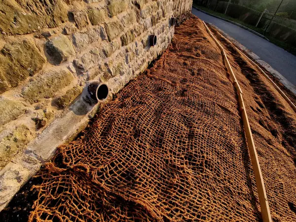 Çimento karıştırıcısının uzun düz duvarı. Duvarın arkasında duvarın içinden drenaj borularıyla çıkarılan toprak var. Kanalizasyon borusu çekiliyor. İnşaat alanı, mezarlık, gabion.