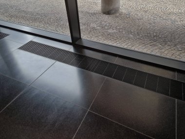 Ofis odasının penceresinin altındaki yerden havalandırma ya da ısıtma gideri. Her şey zeminin altında saklı. Isıtma elemanı vitrinde yer kaplamaz. Minimalist villa ısıtma çözeltisi