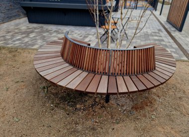 Tahtadan yapılmış yuvarlak bank bir ağacı çevrelemiş, ahşap panellerle oturuyormuş. Metal çerçeve Ağacın etrafındaki tahtalardan oluşan bölümler. Köklerdeki havalandırma ve sulama şebekeleri