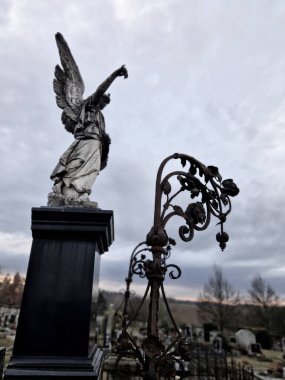 Elinde zil olan dişi bir meleğin heykeliyle süslenmiş anıtsal bir mezar. Özgürlük Anıtı tarzı. Fener asmak için metal süs. Çelik üzerinde porselen güvercin.