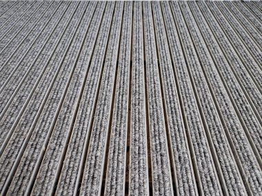 Keçeli mendil, kaset fırçası, gri alüminyum. Profiller asfalt seviyesinin altına gömülmüş. Değiştirilebilir keçeli kalemler ayakkabıları temizler ve suyu emer. Kayma riski azaldı.