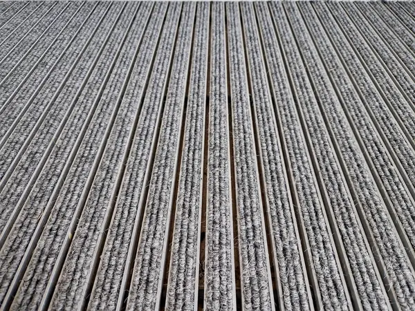 Keçeli mendil, kaset fırçası, gri alüminyum. Profiller asfalt seviyesinin altına gömülmüş. Değiştirilebilir keçeli kalemler ayakkabıları temizler ve suyu emer. Kayma riski azaldı.