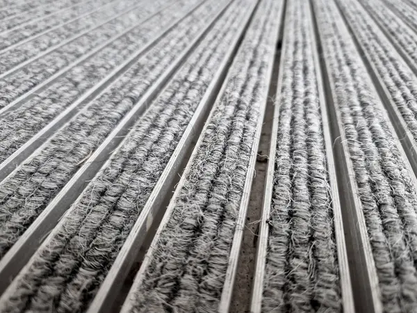 Keçeli mendil, kaset fırçası, gri alüminyum. Profiller asfalt seviyesinin altına gömülmüş. Değiştirilebilir keçeli kalemler ayakkabıları temizler ve suyu emer. Kayma riski azaldı.