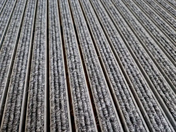 Keçeli mendil, kaset fırçası, gri alüminyum. Profiller asfalt seviyesinin altına gömülmüş. Değiştirilebilir keçeli kalemler ayakkabıları temizler ve suyu emer. Kayma riski azaldı.