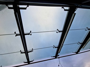 Bina girişinin üstündeki asma cam çatı. Otobüs durağı alüminyum inşaat pergola üzerinde pencereler, otobüs durağı camlı. Metal yapıya birkaç noktada cam tepe örtüsü bağlanmış.