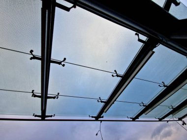 Bina girişinin üstündeki asma cam çatı. Otobüs durağı alüminyum inşaat pergola üzerinde pencereler, otobüs durağı camlı. Metal yapıya birkaç noktada cam tepe örtüsü bağlanmış.