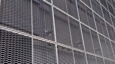Genişletilmiş metal kafes yapısı olan bir binanın çelik kaplaması. Galvanize gri ağlar endüstriyel binayı koruyor. Gümüş arkaplan, duvar, çizgi, astarın aksine mavi gökyüzü