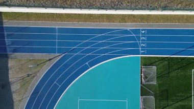 Birkaç şeritli koşu pisti olan bir spor stadyumu. Oval Ofis 'te netbol ve hentbol için kalkan engelleri olan küçük bir futbol sahası var. Sentetik bölge. Yukarıdan manzara, tüm hava koşulları, kauçuk, 