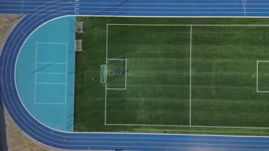 Birkaç şeritli koşu pisti olan bir spor stadyumu. Oval Ofis 'te netbol ve hentbol için kalkan engelleri olan küçük bir futbol sahası var. Sentetik bölge. Yukarıdan manzara, tüm hava koşulları, kauçuk, 