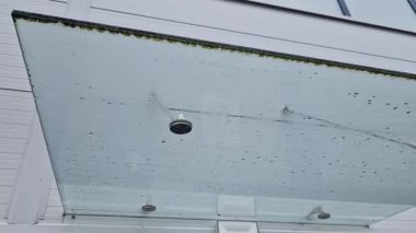 Girişteki cam çatı, metal kaplamalı endüstriyel bina. Kalın duvarlı cam panel, metal çubukların üzerinde asılı. Yuvarlak hedef tutucular, buzlu, paslanmaz çelik, mavi.