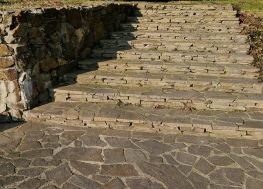 Sabah güneşiyle aydınlatılan taş merdiven. Taş kahverengidir ve çimento harcı ile birleştirilmiştir. Merdivenler kayalık bahçede ya da parkta.