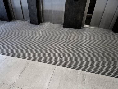 Keçeli mendil, kaset fırçası, gri alüminyum. Profiller asfalt seviyesinin altına gömülmüş. Değiştirilebilir keçeli kalemler ayakkabıları temizler ve suyu emer. Kayma riski azaldı.