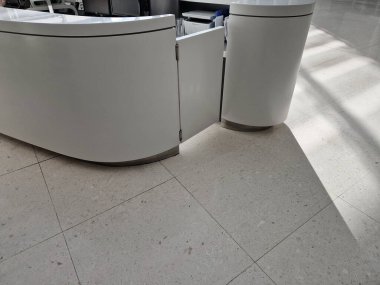 Resepsiyon masasının girişinde yay menteşeli sallanan kapı. Tezgahın yuvarlak hatlarına bakan korian.