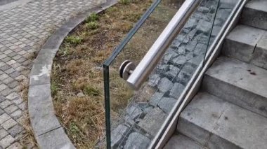 Cam korkuluklar paslanmaz çelik boru çerçevesine yapışmış ve vidaların yardımıyla yapıştırılmış güvenlik camına bağlanmış. Arka planda otlar olan bir çiçek tarhı, çatı bahçesi terası