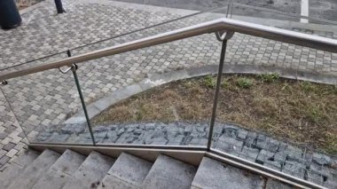 Cam korkuluklar paslanmaz çelik boru çerçevesine yapışmış ve vidaların yardımıyla yapıştırılmış güvenlik camına bağlanmış. Arka planda otlar olan bir çiçek tarhı, çatı bahçesi terası