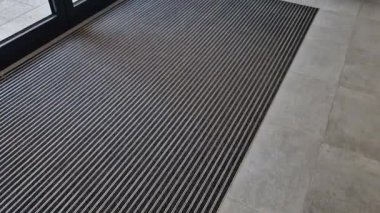 Binanın girişindeki endüstriyel paspas temizleme bölgeleri. Kemer ya da yarım daire şeklinde siyah plastik bir minder kireçtaşı mozaik fayansların üzerinde yatar.