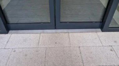 Binanın girişindeki endüstriyel paspas temizleme bölgeleri. Kemer ya da yarım daire şeklinde siyah plastik bir minder kireçtaşı mozaik fayansların üzerinde yatar.