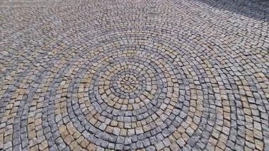 Meydanda katlanmış taşlar, gri granit kaldırımın ortasında daha büyük bir fayansla daireler çiziyor. Suyun üzerindeki daireler kaldırımın simgesidir. Büyük ve küçük harmanlanmış.