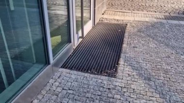 Binanın girişindeki endüstriyel paspas temizleme bölgeleri. Kemer ya da yarım daire şeklinde siyah plastik bir minder kireçtaşı mozaik fayansların üzerinde yatar.