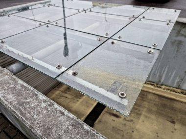 Yeraltı garajının çıkışının üstündeki cam çatı. Katı koruyucu cam levhayı delip geçen vidalarla tutulur. galvanize çerçeveden pergola