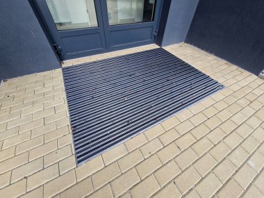 Keçeli mendil, kaset fırçası, gri alüminyum. Profiller asfalt seviyesinin altına gömülmüş. Değiştirilebilir keçeli kalemler ayakkabıları temizler ve suyu emer. Kayma riski azaldı.