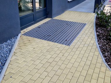 Keçeli mendil, kaset fırçası, gri alüminyum. Profiller asfalt seviyesinin altına gömülmüş. Değiştirilebilir keçeli kalemler ayakkabıları temizler ve suyu emer. Kayma riski azaldı.